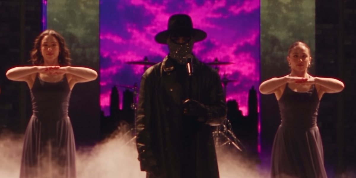 The masked singer centre stage, between two dancers, in Safety - The Musical